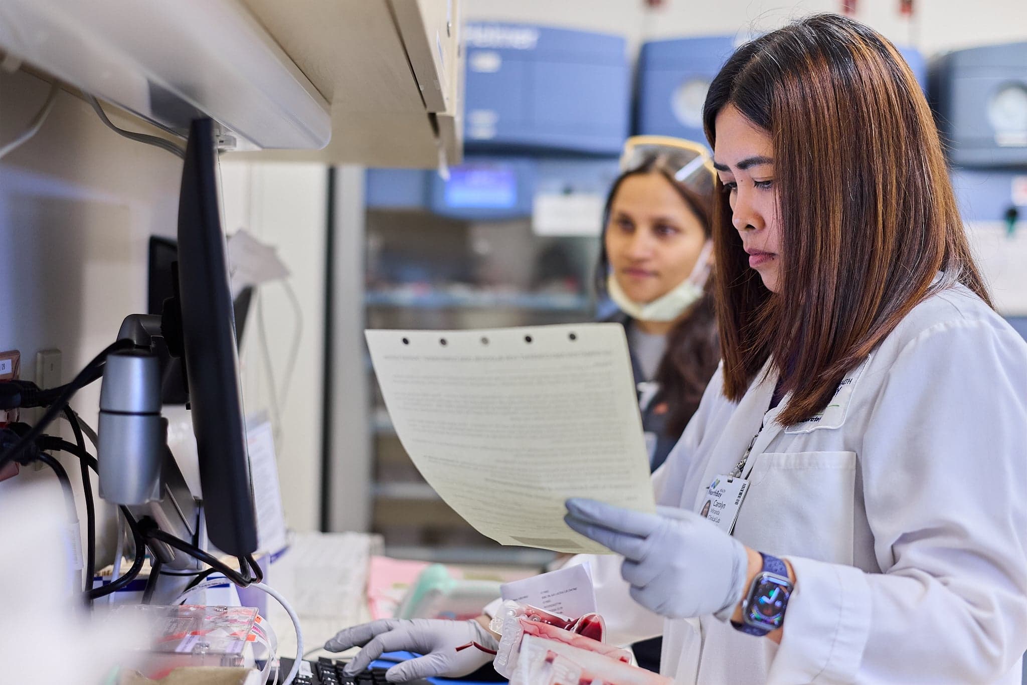 A medical provider in a lab entering information into a computer from a document.