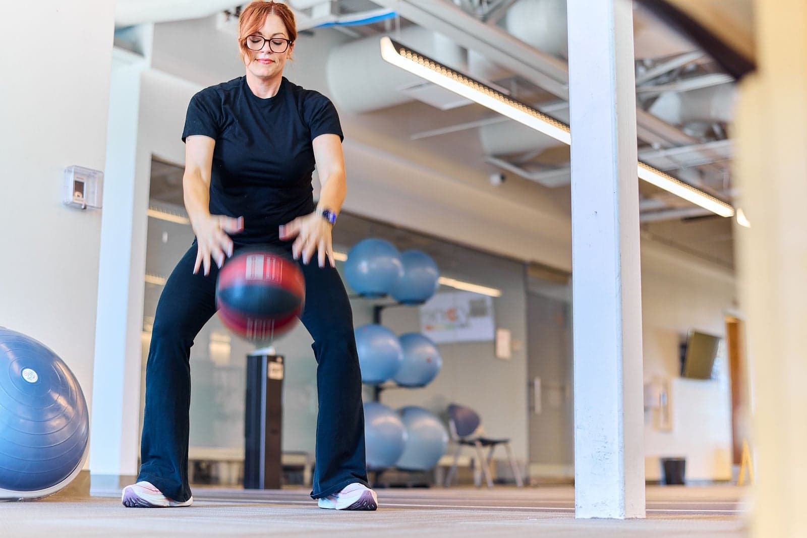 A woman squats while bouncing a weighted ball in a rehabilitation gym.