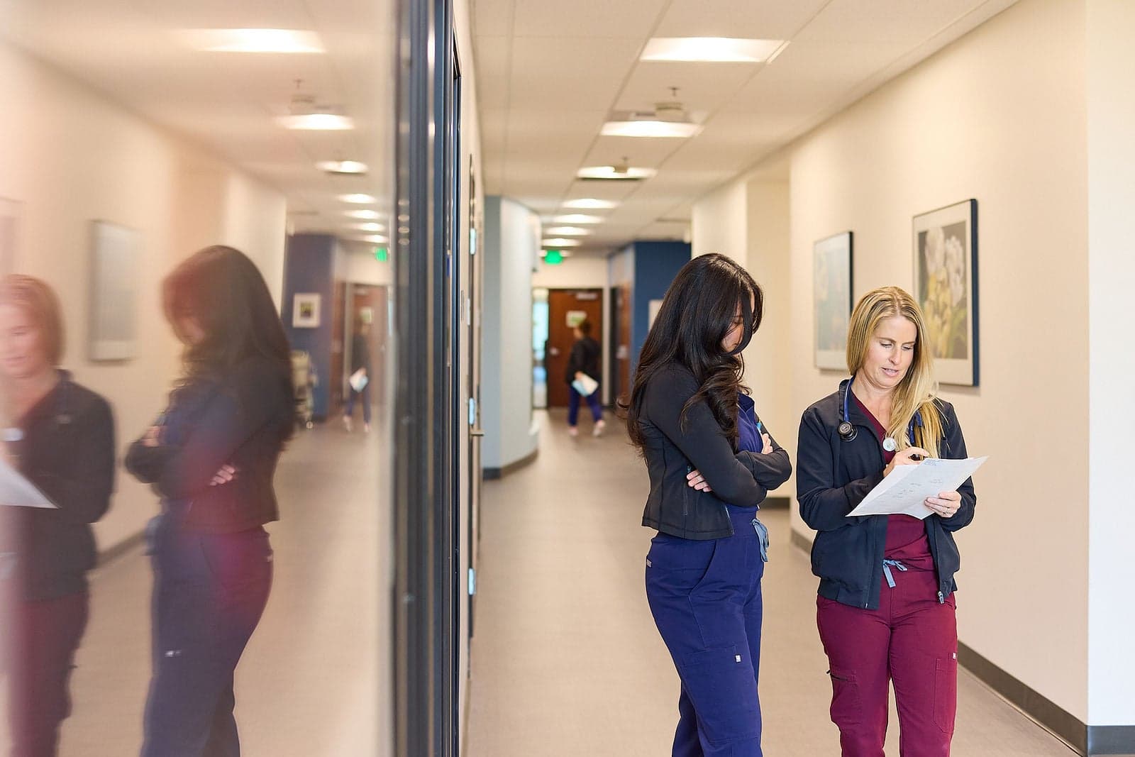Two clinicians review a document together in a hospital hallway.