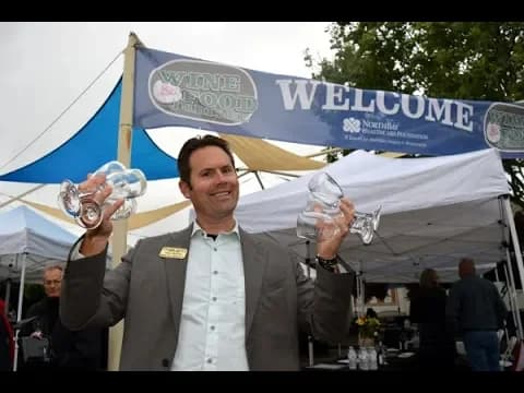 Man holding two glass awards at outdoor event with Welcome banner and tent in background