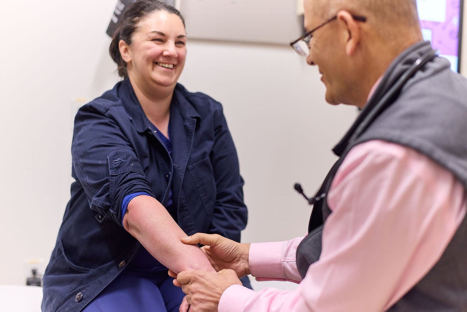 A smiling woman holds out her arm as a Northbay Health doctor checks it in an exam room.