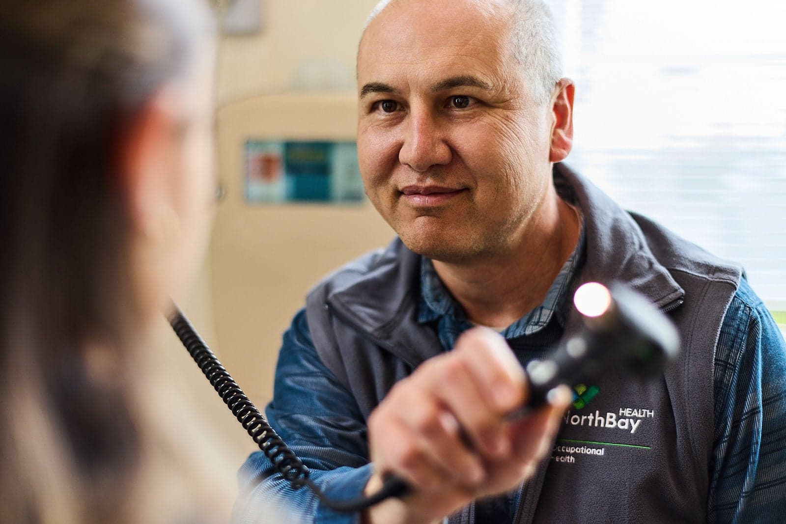 A Northbay Health clinician holds an exam instrument while facing a patient.