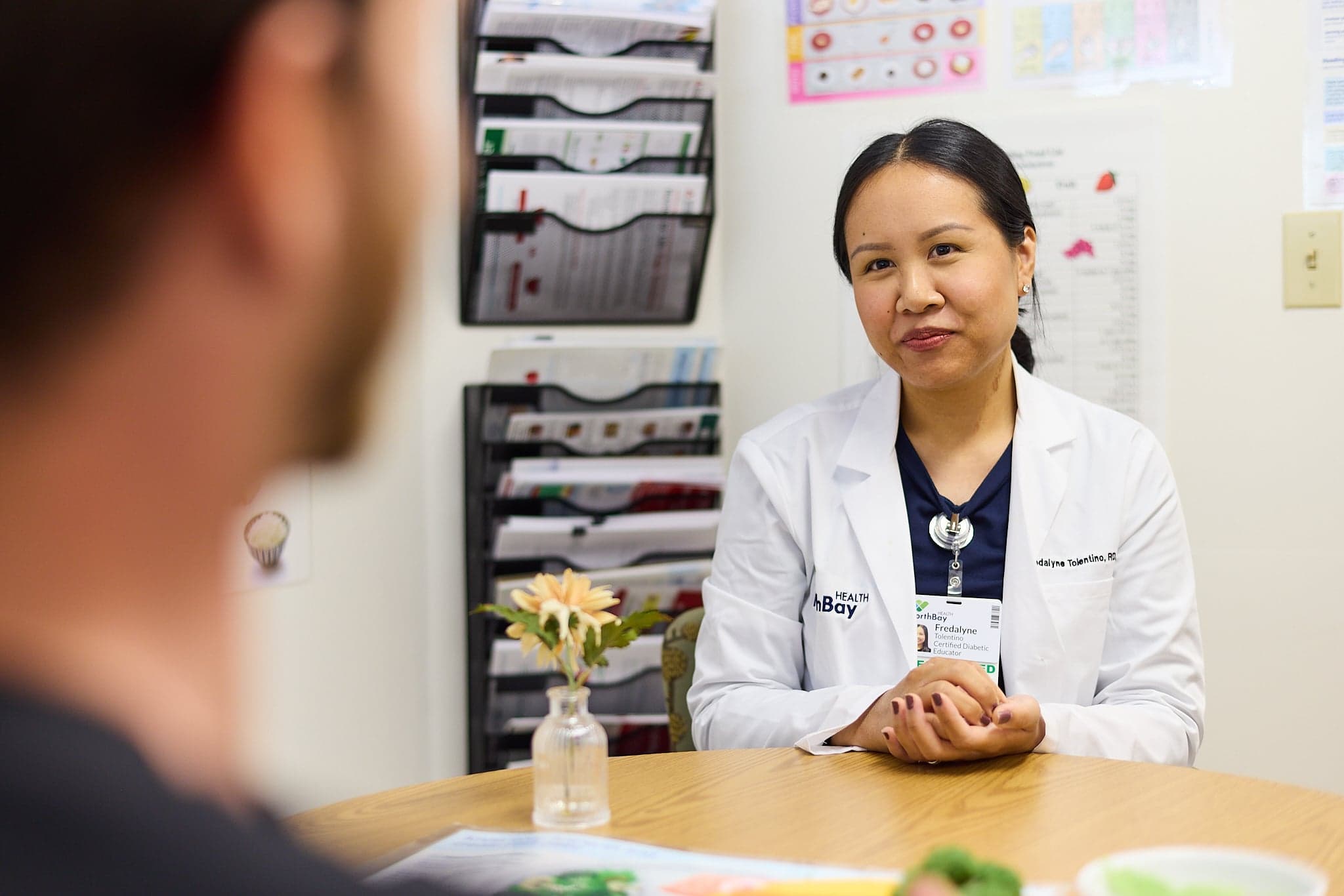 A female dietitian speaks with a patient while seated at her desk.