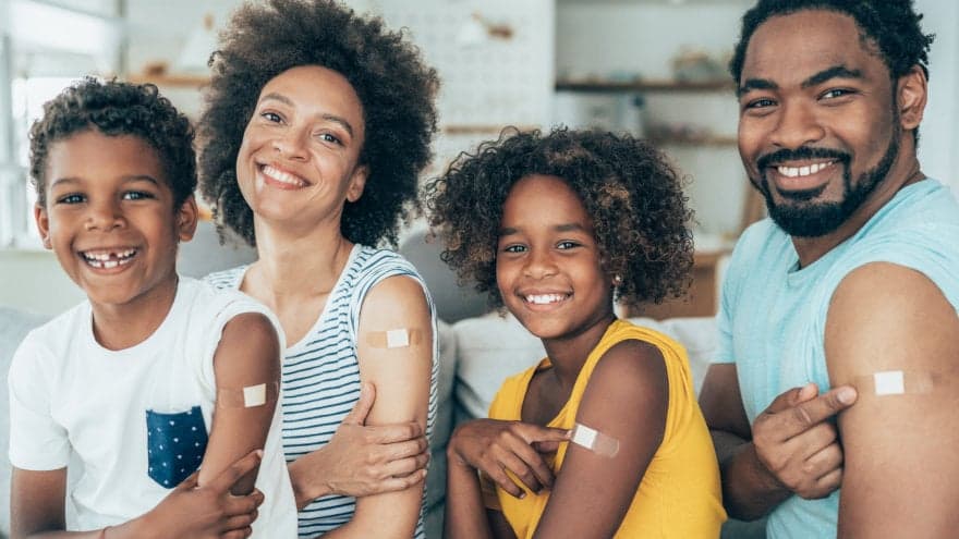 A whole family showing off the bandages on their arm after receiving their initial dose or 3rd dose booster.