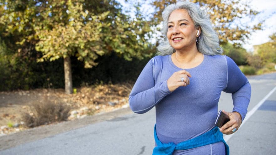 Mature woman with long grey hair jogging on a country road.