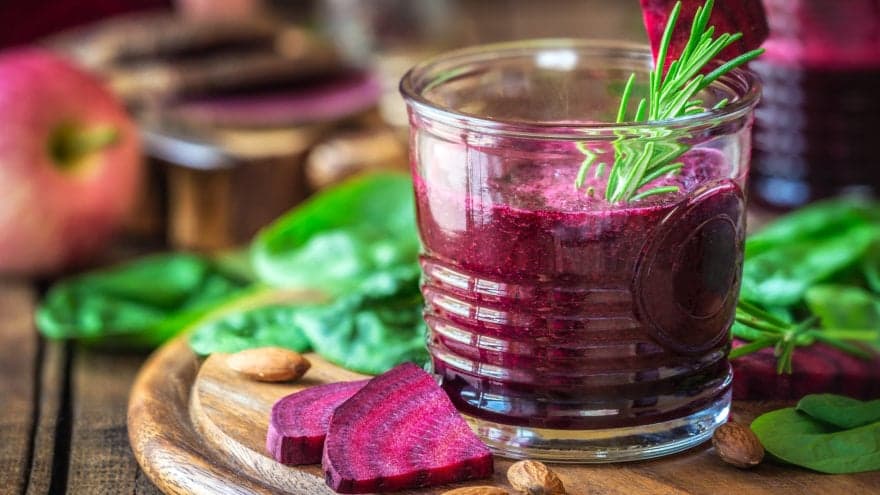 A close-up shot of a berry smoothie in a glass on a table with spinach.