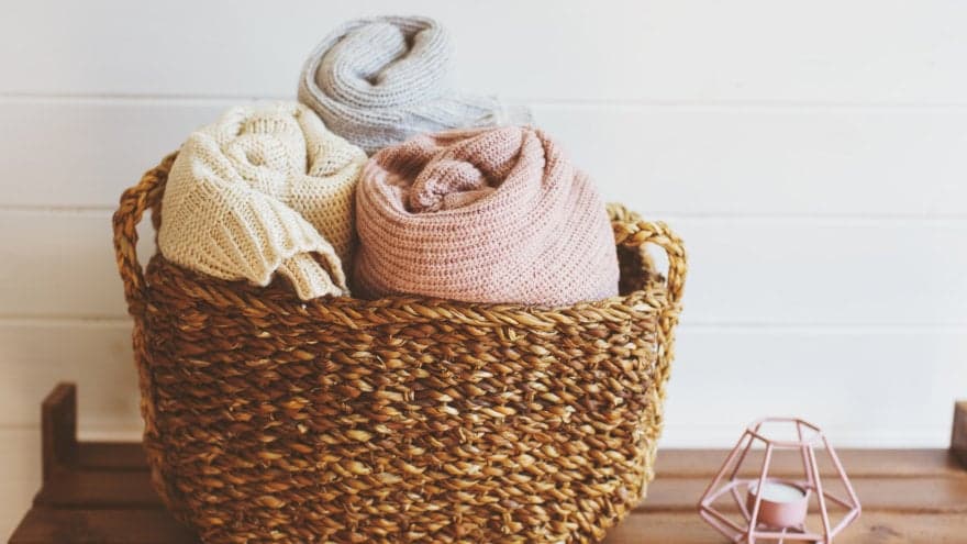 A basket filled with three blankets with a candle next to it.