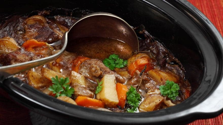 Close up of Irish stew where chunks of browned meat and thick cut vegetables can be seen. A soup ladle cuts through the middle, showing its rich broth.