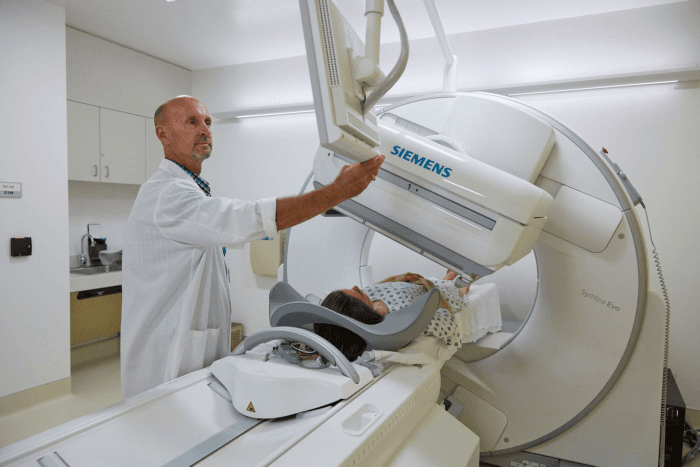 A staff member adjusts a nuclear medicine gamma camera over a patient lying on the scanner table.